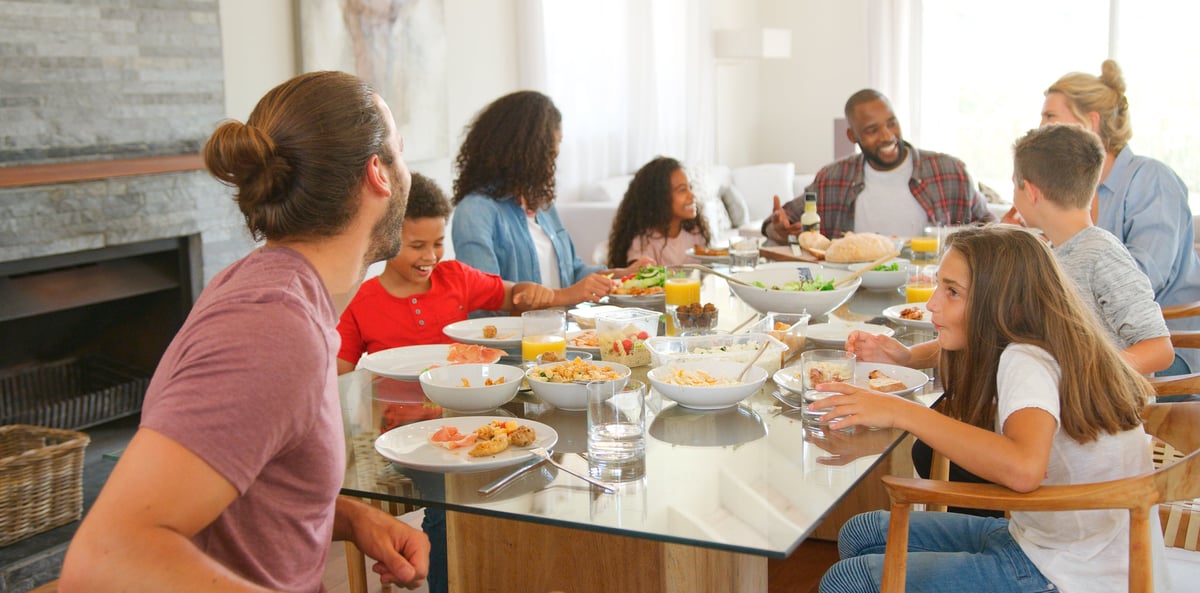 Two families sitting around table together enjoying meal at home