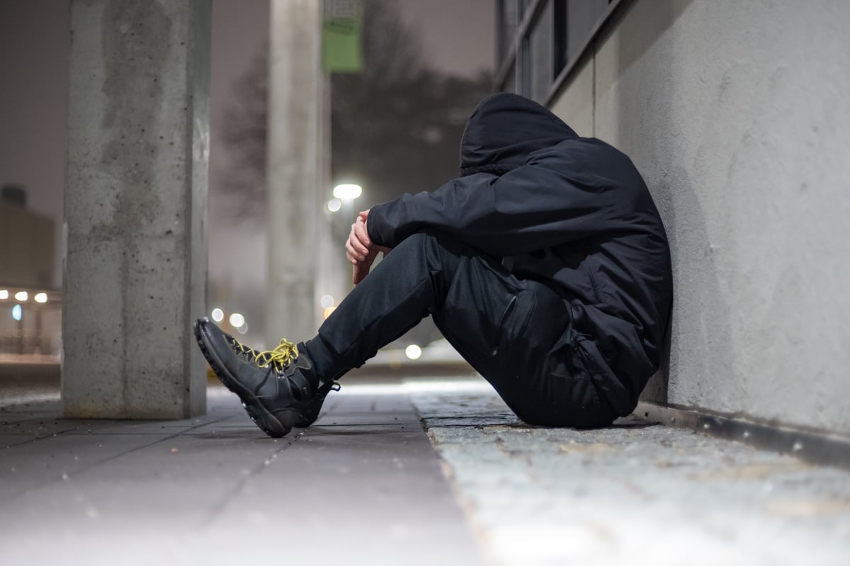 Depressed hooded man sitting on a street during night time