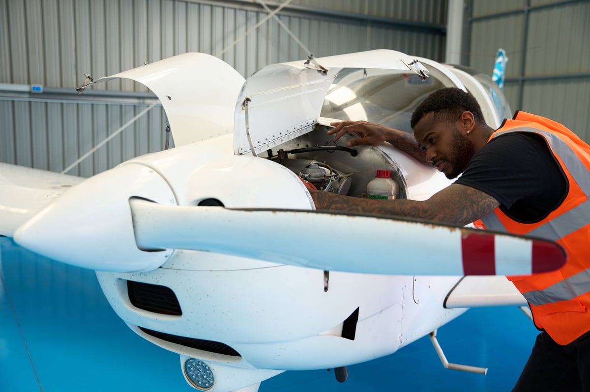 Young man working diligently as an aircraft mechanic inspecting the engine of a small airplane inside a spacious hangar