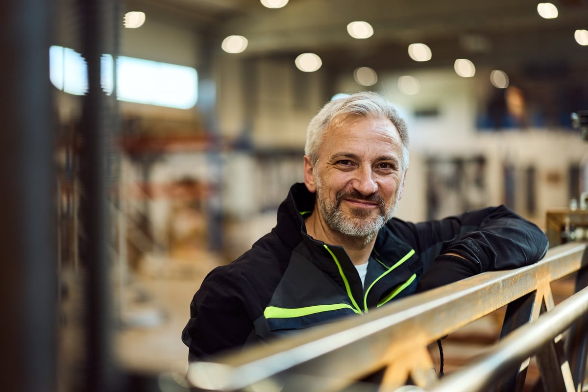 Confident mature man in an industrial environment leaning on equipment with a smile