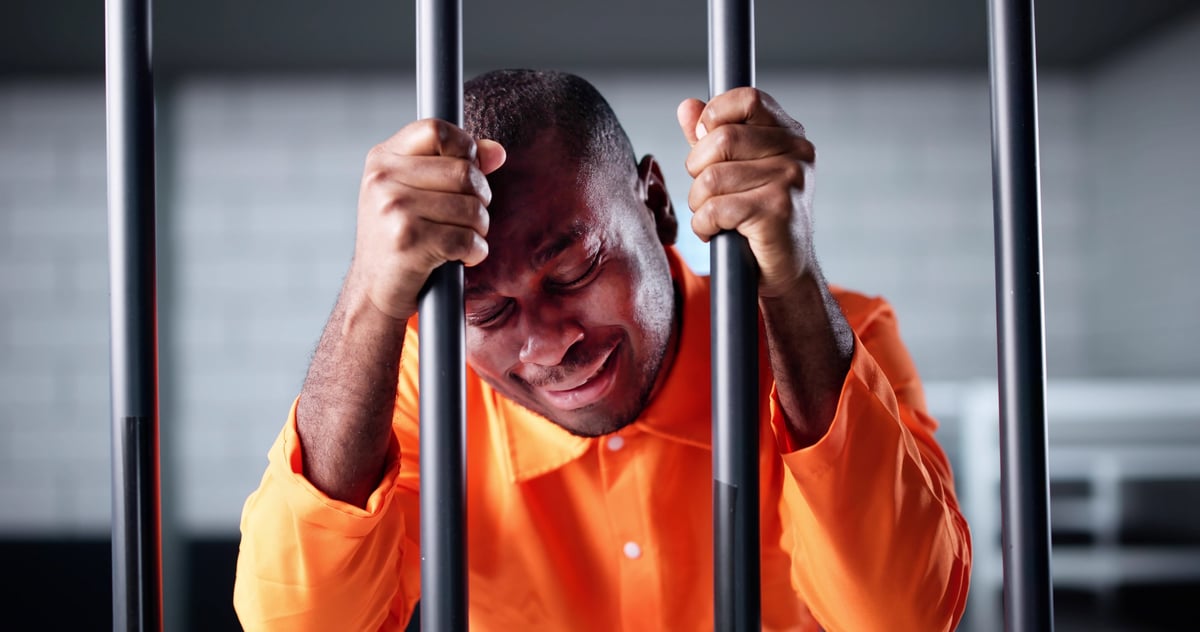 Sad African American man behind bars in jail cell