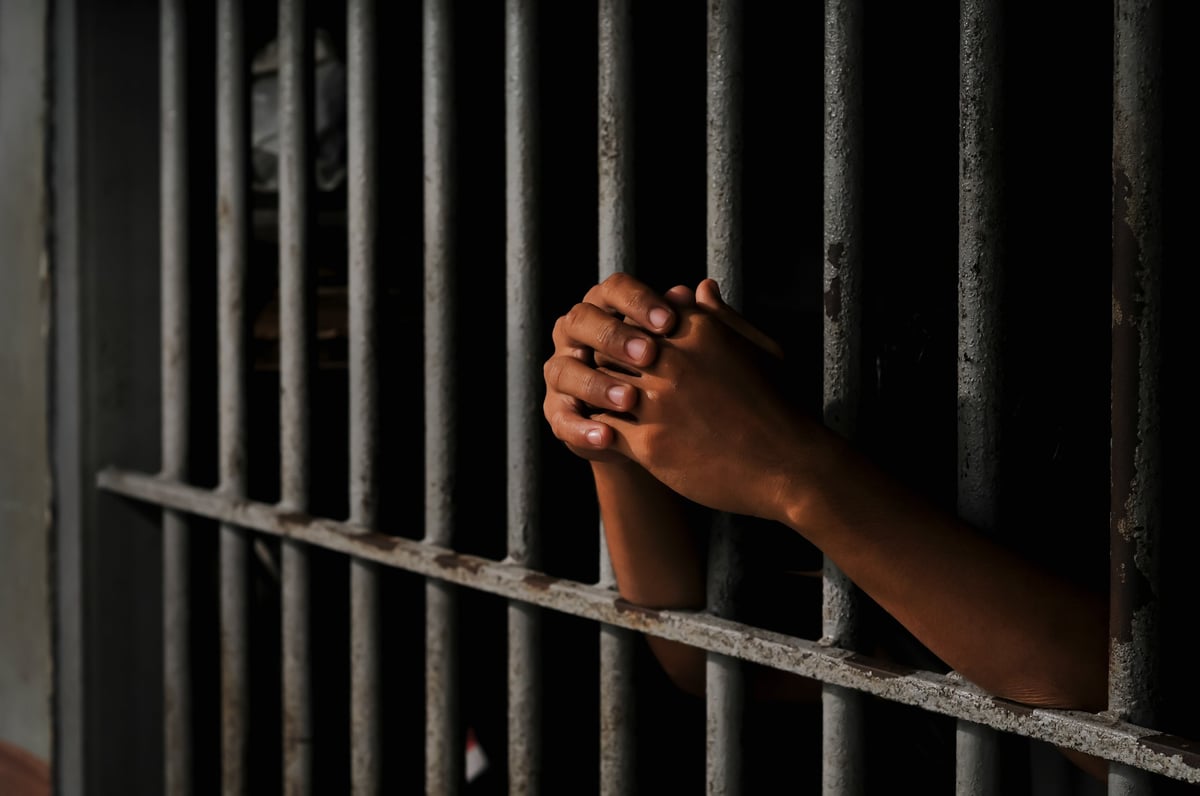 Close-up of an inmate's hand holding prison bars in a dark cell