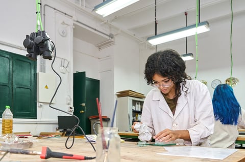 Focused young woman wearing a lab coat and safety glasses, meticulously working on an artistic glass craft project in a studio.