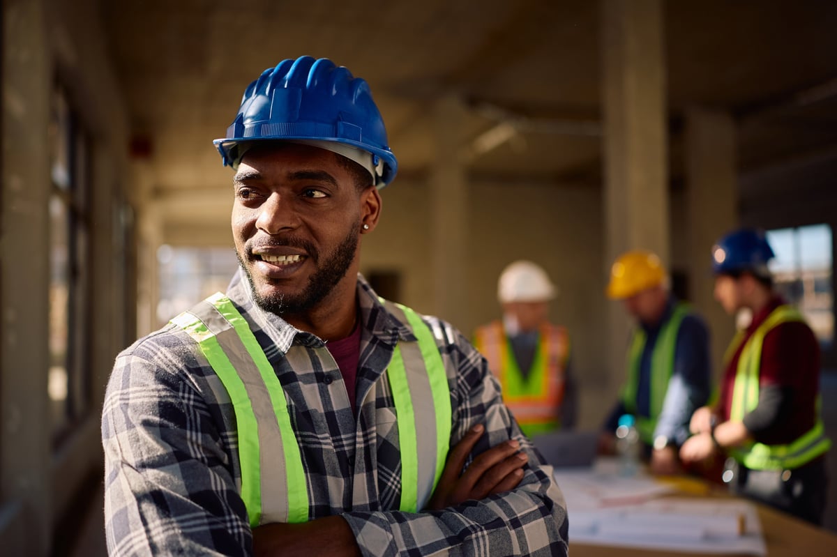 Happy African American worker standing with crossed arms at construction site and looking away